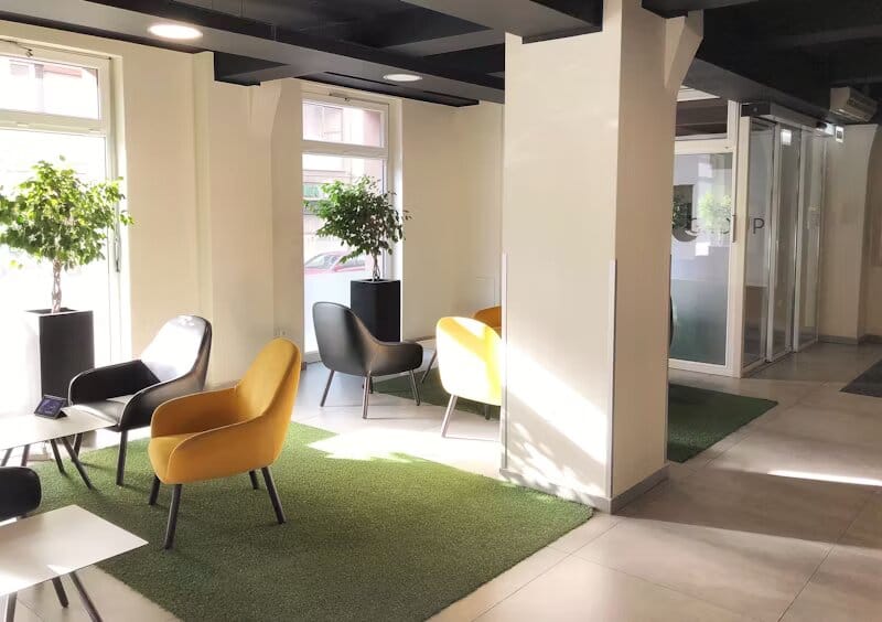 one de détente lumineuse dans un centre d'affaires avec des fauteuils colorés, des tapis verts et des plantes décoratives près de grandes fenêtres.